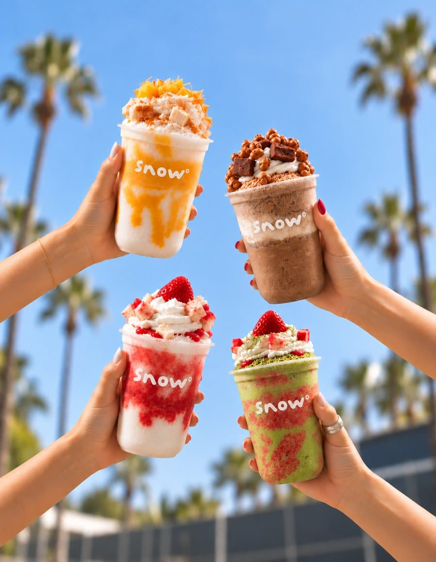 Four Snow° cups held up against palm trees and blue sky